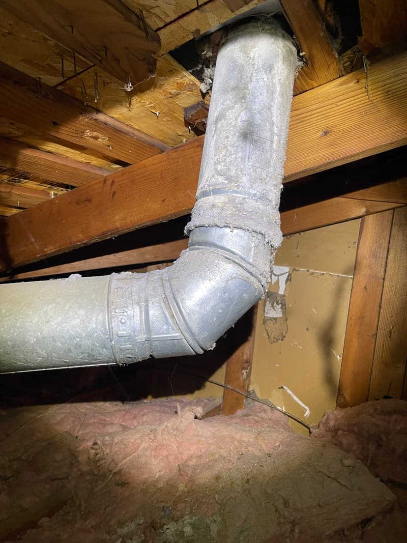 Cluttered area behind dryer with lint, dust, and vent hose