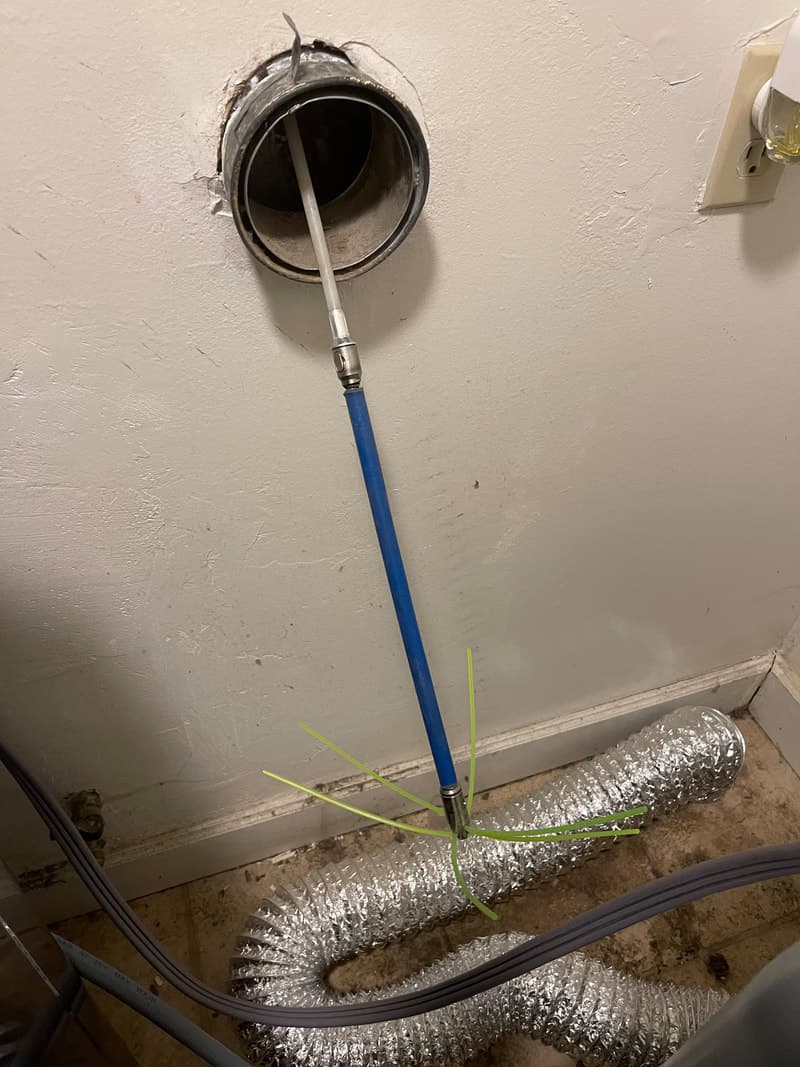 Rooftop dryer vent cleaning in progress with green cleaning rod